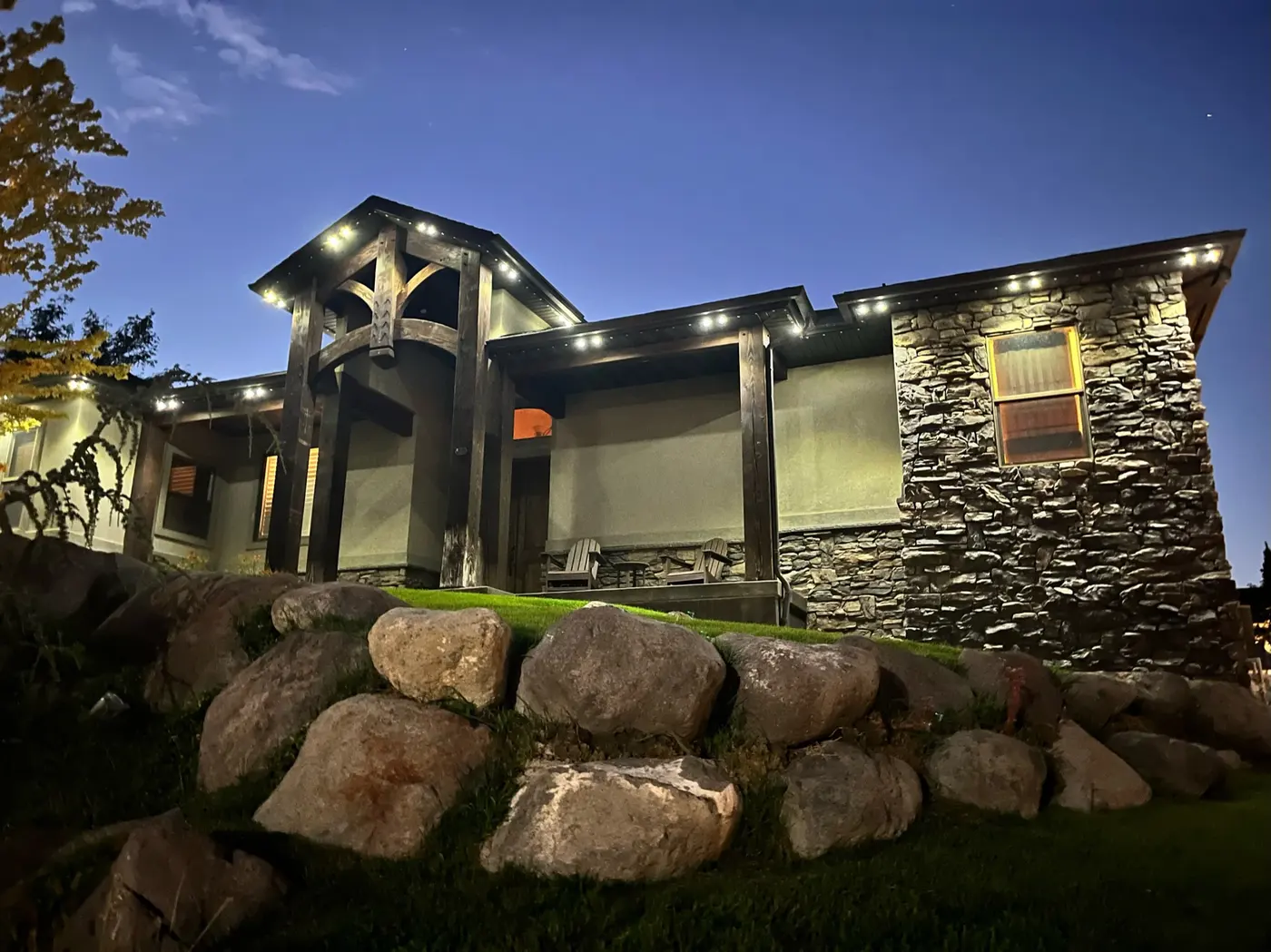 Stone mountain home with downlit eaves at dusk